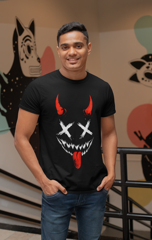 A smiling man wearing a black t-shirt with a red and white Hannya demon mask illustration featuring X's for eyes, sharp teeth, red horns, and a tongue sticking out. He has his hands in his pockets and is standing indoors.