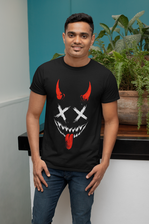 A smiling man wearing a black t-shirt with a red and white Hannya demon mask illustration featuring X's for eyes, sharp teeth, red horns, and a tongue sticking out. He has his hands in his pockets and is standing indoors.