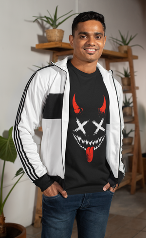 A smiling man wearing a black t-shirt with a red and white Hannya demon mask illustration featuring X's for eyes, sharp teeth, red horns, and a tongue sticking out. He has his hands in his pockets and is standing indoors.
